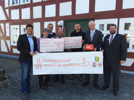 Herbert Klein (Mi.) überreichte jetzt die beiden Schecks über jeweils 1.500 Euro an Kai Langenbach (3.v.r.) und Pfarrerin Daniela Walter (2.v.l.). Mit dabei: Johannes Werthenbach von der Gemeinde Burbach, Rolf Dzubiel, Vorsitzender MGV „Eintracht“ Burbach, Bürgermeister Christoph Ewers und Michael Seyfarth von der Sparkasse Burbach-Neunkirchen. (Foto: Gemeinde Burbach)