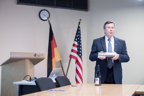 Stephen A. Hubler bei seinem Vortrag "The Art of Diplomacy and the Importance of Intercultural Awareness" im Senatssaal der Universität Siegen. Kulturelle Unterschiede zwischen USA und EU werden auch an Alltagsgegenständen wie Buchumschlägen oder Flaschen-Etiketten deutlich. (Foto: Uni)