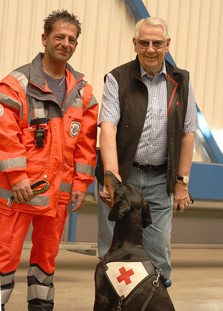 Unternehmer Klaus Vetter (rechts) unterstützt gerne das ehrenamtliche Engagement seiner Mitarbeiter wie Roger Merte (links), der sich mit seiner Dobermannhündin Chandra zurzeit intensiv auf die Einsatzprüfung zum DRK-Rettungshundeteam vorbereitet und mit den Kameraden der Siegen-Wittgensteiner DRK-Rettungshundestaffel an seinem Arbeitsplatz trainieren durfte. (Foto: DRK)