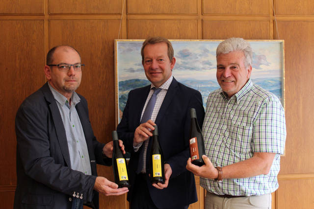 Die Vorstandsmitglieder des Siegerländer Weinkonvents, Michael Dickel (links) und Wolfgang Narjes (rechts), überreichten Bürgermeister Steffen Mues Wein aus heimischem Anbau. Die Stadt Siegen gibt die raren Tropfen als besondere Geschenke weiter. (Foto: Stadt Siegen)